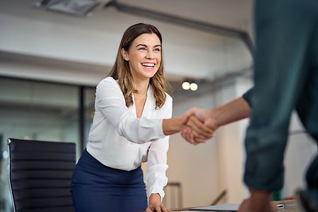 Happy mid aged business woman manager handshaking greeting client in office.