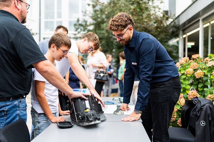 Viele junge Menschen stehen an einem Tisch und schauen sich Technik an