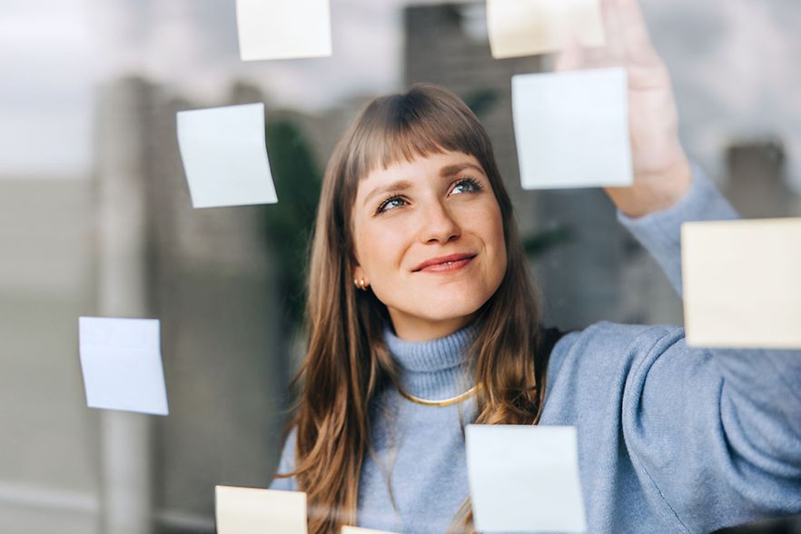 Junge Unternehmerin bringt Post-its an einer Glaswand an