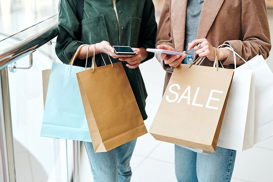 Hands of two young contemporary shoppers with smartphones and paperbags