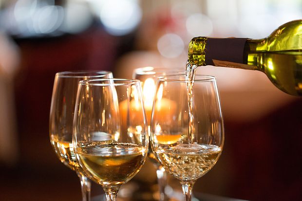 Jemand schenkt Weißwein in Gläser