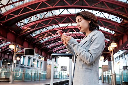 Businesswoman traveling, using phone while waiting at train station