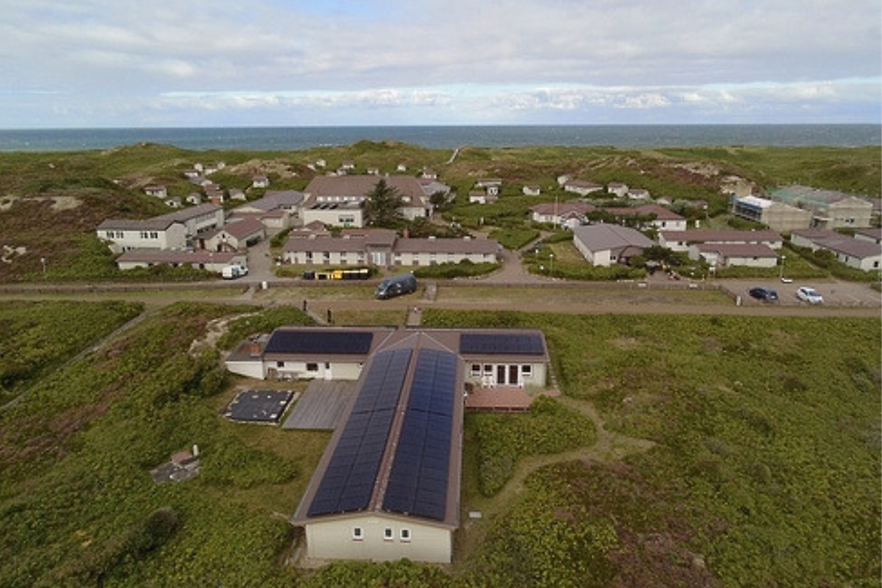 Luftaufnahme eines l&auml;nglichen Geb&auml;udes in den D&uuml;nen mit Photovoltaik