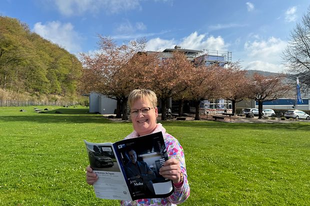 Eine Frau steht auf einer Wiese und liest in einer Zeitschrift.