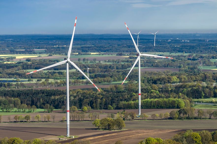 Das Foto zeigt einen Windpark. Windr&auml;der befinden sich auf einer Gr&uuml;nfl&auml;che.
