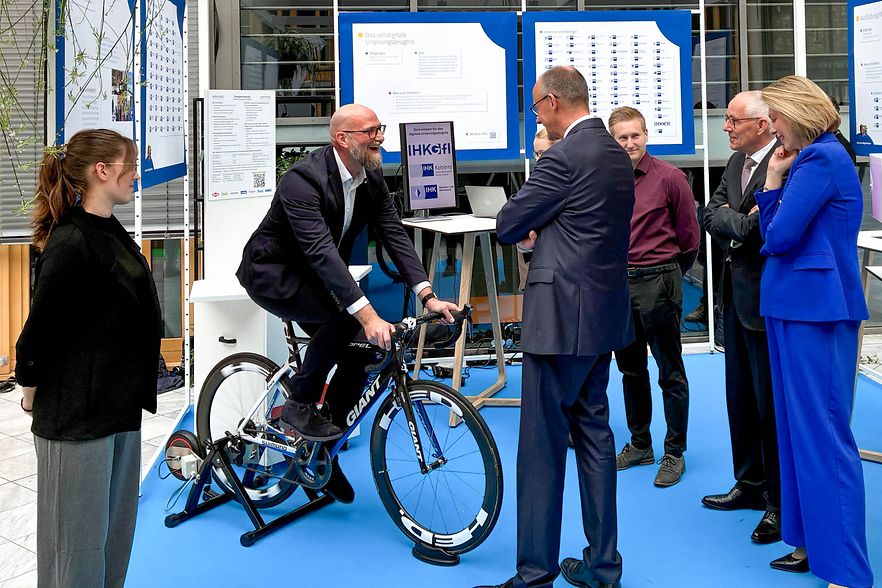 Person auf Rennrad spricht mit Gruppe an Messestand der IHK