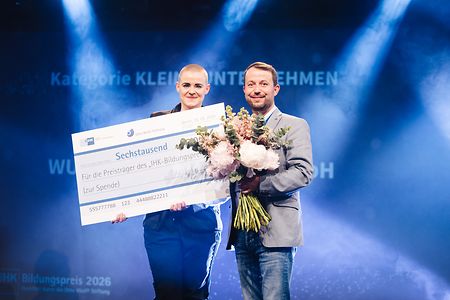 Personen stehen auf der B&uuml;hne und halten einen Scheck und Blumen in der Hand