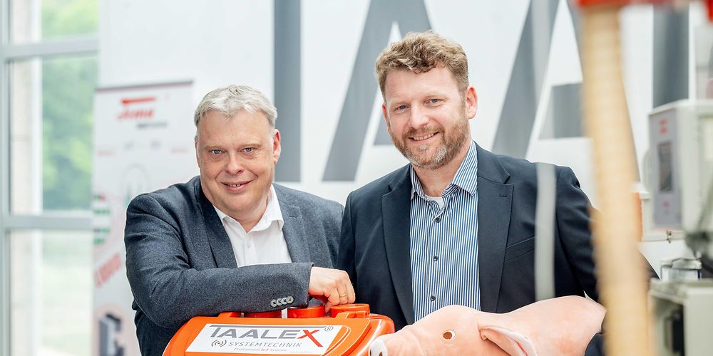 Zwei M&auml;nner hinter einer Maschine f&uuml;r Landwirtschaft, mit einem Pl&uuml;schschwein.