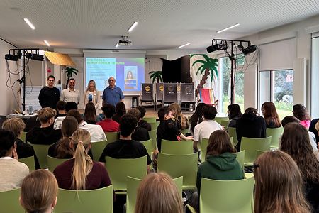 Lehrer der Schule und Dame von IHK stehen vor den Sch&uuml;lern und berichten &uuml;ber die duale Ausbildung