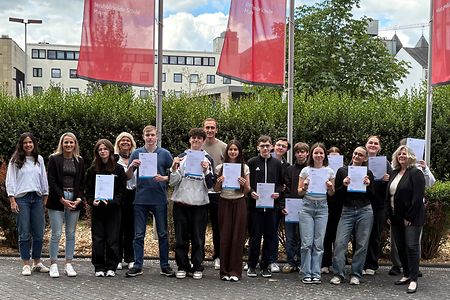 Sch&uuml;ler halten ihre Zertifikate in der Hand und stehen mit Lehrern vor der Schule 