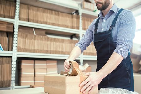 Mann klebt mit Packband ein Paket zu
