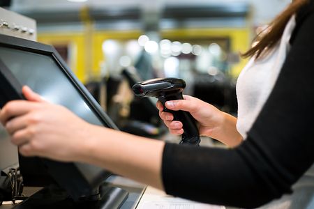 Junge Frau an elektronischem Kassensystem mit Scanner in der Hand