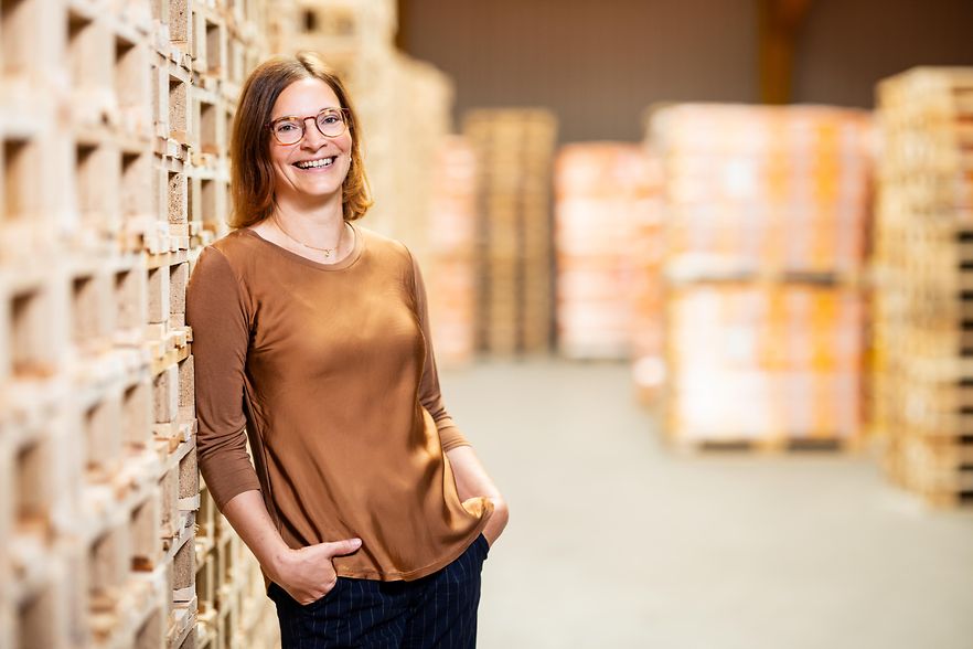 Frau steht l&auml;chelnd vor B&uuml;cherregalen