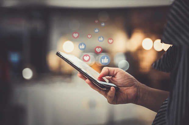 Person fährt mit dem Daumen über ein Mobiltelefon, darüber sind Like-Symbole zu erkennen