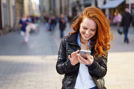 Eine junge Frau steht in einer Einkaufsstra&szlig;e und schaut auf ihr Smartphone