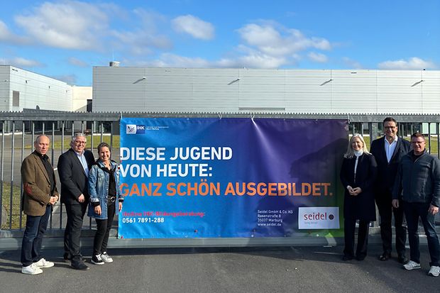 Bauzaun-Banner mit mehreren Personen links und rechts 