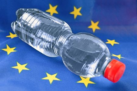 Eine volle Kunststoff-Wasserflasche, ohne Etikett, liegt auf einer EU-Flagge.