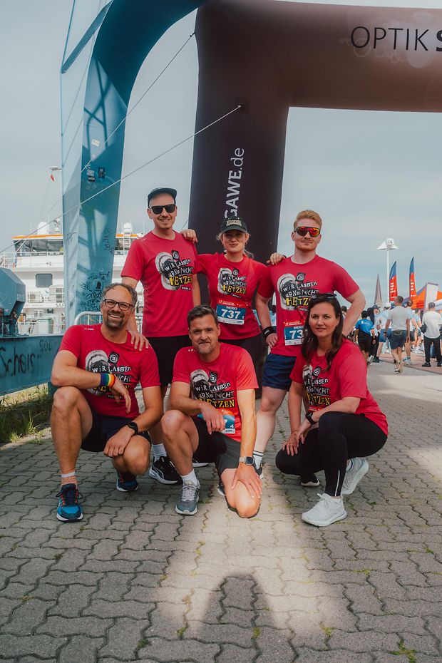 Sechs Menschen posieren am Rostocker Stadthafen in roten Lauf-Shirts.