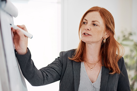 Bei einem Meeting schreibt eine Frau in Businesskleidung Notizen auf ein Flipchart.