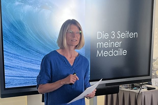 Judith H&ouml;rmann vor einem gro&szlig;en Bildschirm mit der Aufschrift: Die 3 Seiten meiner Medaille