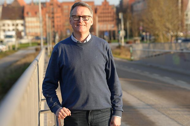 Ein Mann steht auf einer Br&uuml;cke und l&auml;chelt in die Kamera