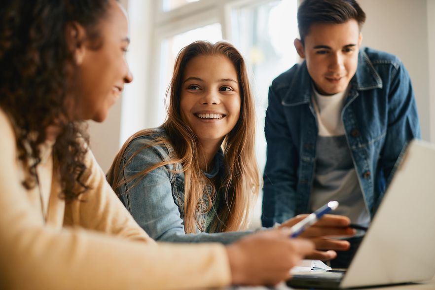 Drei Sch&uuml;ler der Berufschule sitzt vor einem Laptop und sind im Gespr&auml;ch.