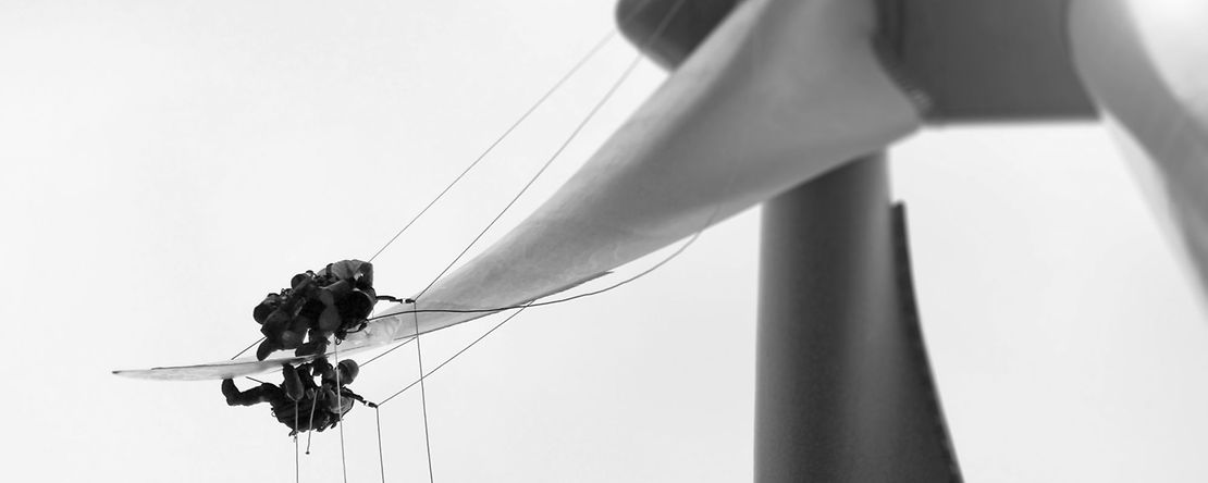 Zwei Personen reparieren den Fl&uuml;gel eines Windrades