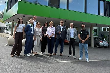 Eine Personengruppe steht vor einem Firmengeb&auml;ude.