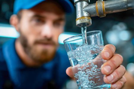 Technician fills a glass with clean water while checking filtration system performance