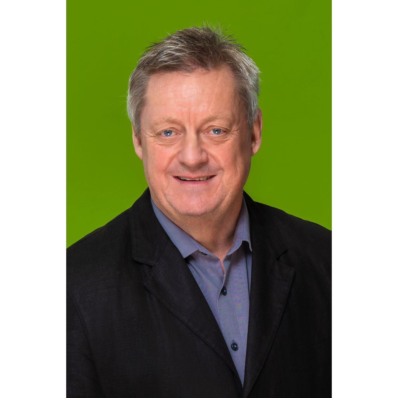 Porträt einer Person im dunklen Sakko und Hemd vor einem grünen Hintergrund.