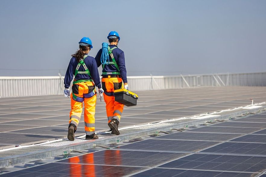 zwei Personen in auff&auml;lliger Kleidung auf dem Dach mit PV-Anlagen