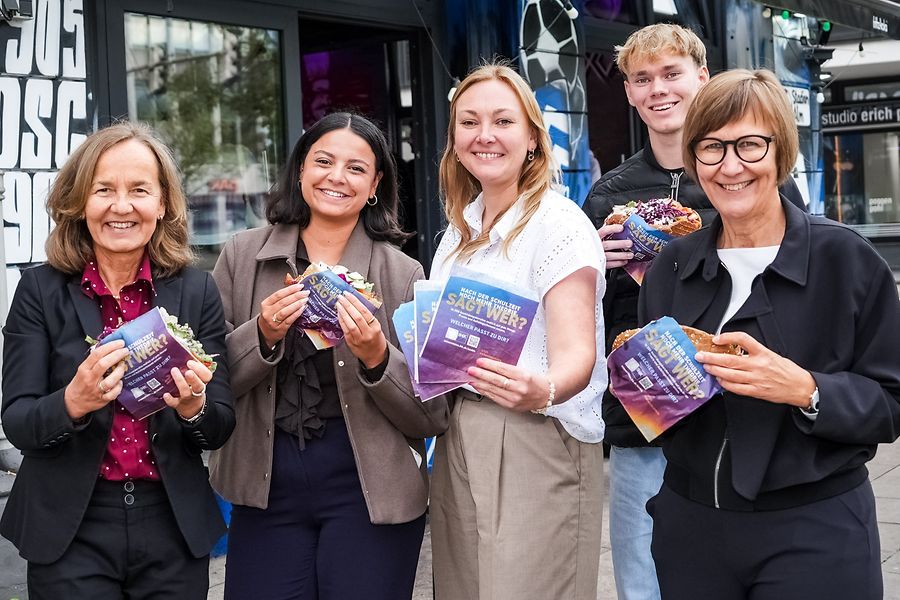 Fünf Menschen halten Dönertüten und essen Döner vor einem Geschäft.