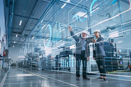 Zwei Industrieingenieure nutzen einen Tablet-Computer und visualisieren eine Wand mit Big-Data-Statistiken.