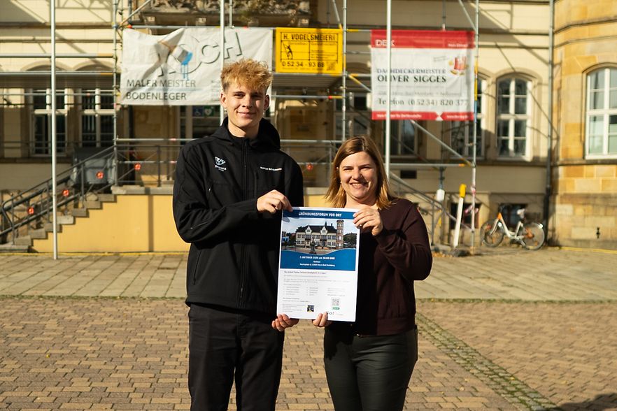 Das Foto zeigt zwei Menschen mit einem Plakat als Werbung f&uuml;r das Gr&uuml;ndungsforum