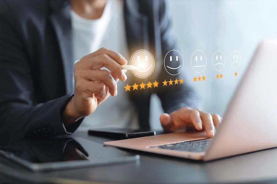 Person bewertet digitale Kundenzufriedenheit am Laptop mit einer F&uuml;nf-Sterne-Bewertung und Feedback-Symbolen.