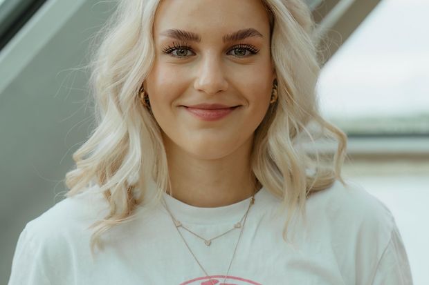 Eine junge Frau mit blonden Haaren l&auml;chelt in die Kamera. Sie tr&auml;gt ein T-Shirt mit der Aufschrift Basketball macht Schule.