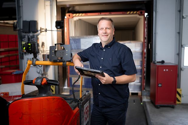 Ein Mann steht in einer Logistikhalle mit einem Tablet in der Hand