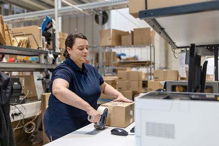 Frau packt ein Paket mit Klebeband im Lager
