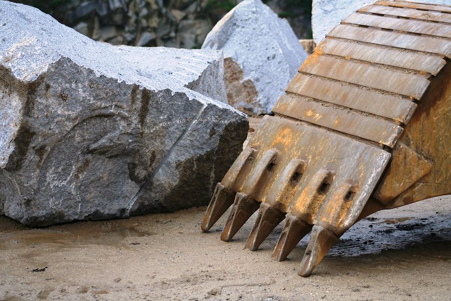 Baggerl&ouml;ffel vor gro&szlig;en Felsbl&ouml;cken in einem Steinbruch.