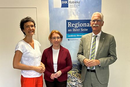 Zwei Frauen und ein Mann stehen nebeneinander vor einem Rollup