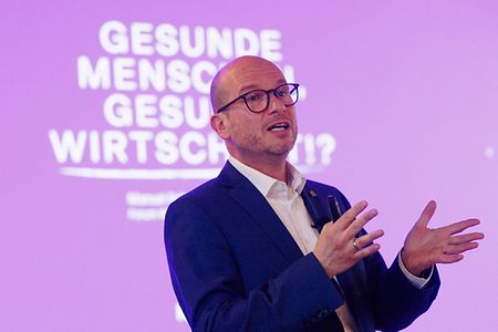 Ein Mann vor einen lilafarbigen Leinwand mit Text.