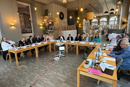 Eine Personengruppe sitzt an einer U-f&ouml;rmigen Tischreihe in einem Restaurant
