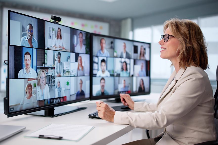 Businessfrau vor 2 Monitoren mit zugeschalteten Teilnehmer eines Webinars